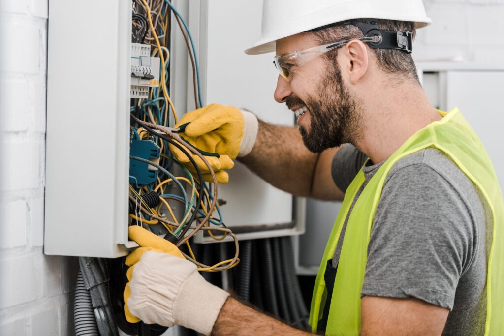 side-view-of-smiling-handsome-electrician-repairing-electrical-box-with-pliers-in-corridor.jpg